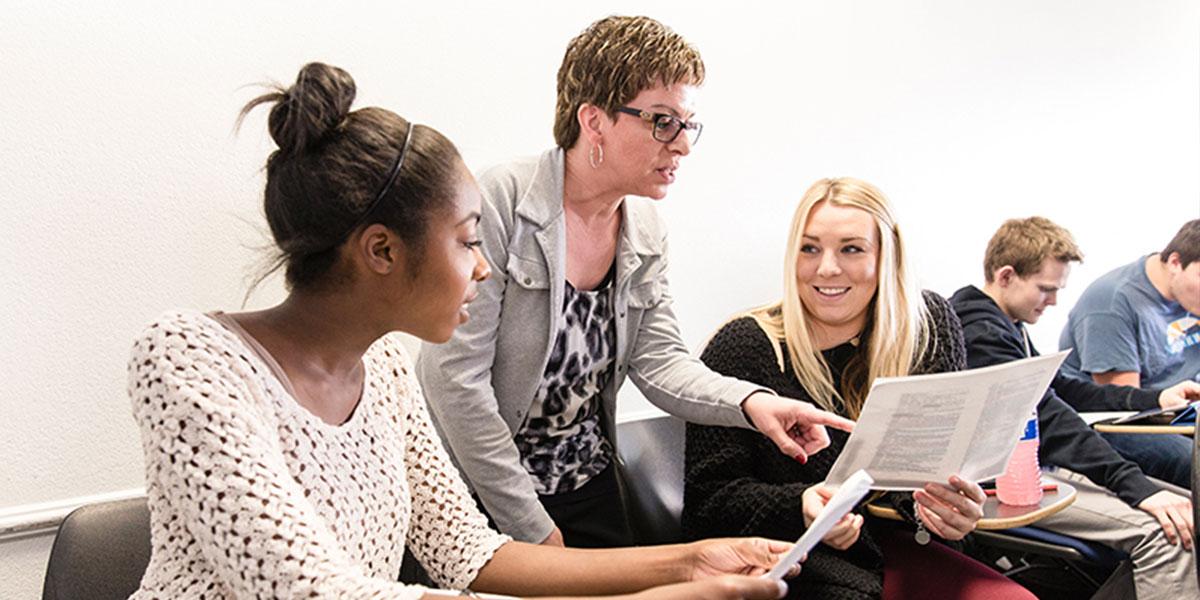 Professor helping two female students with an assignment in class